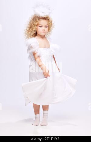 Belle, mignon petite fille enfant en robe blanche à l'image d'ange debout isolé sur fond de studio blanc Banque D'Images