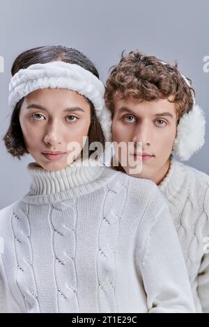jeunes modèles interraciaux dans des vêtements chauds et confortables regardant la caméra sur gris, campagne de mode d'hiver Banque D'Images