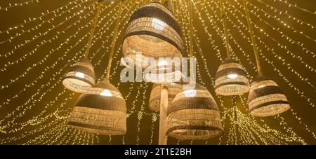 Lampes en fibre naturelle suspendues au plafond d'une tente avec un fond de guirlandes LED. Ambiance chaleureuse Banque D'Images