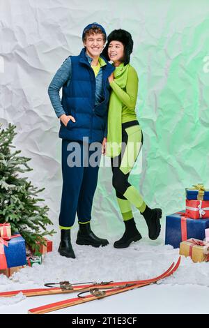 heureux modèles de mode interracial en tenue d'hiver près de l'arbre de noël et cadeaux sur la neige en studio Banque D'Images