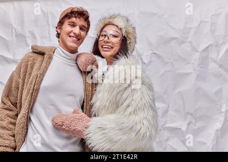 joyeux couple interracial dans des vêtements chauds à la mode sur fond texturé blanc, mode hiver Banque D'Images