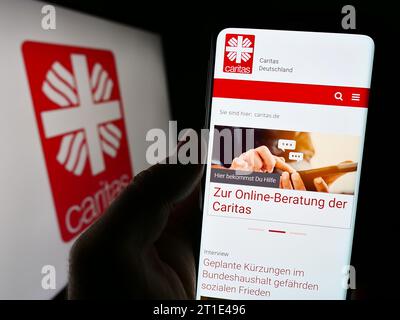 Personne tenant un téléphone portable avec la page Web de l'organisation allemande Deutscher Caritasverband e.V. devant le logo. Concentrez-vous sur le centre de l'écran du téléphone. Banque D'Images