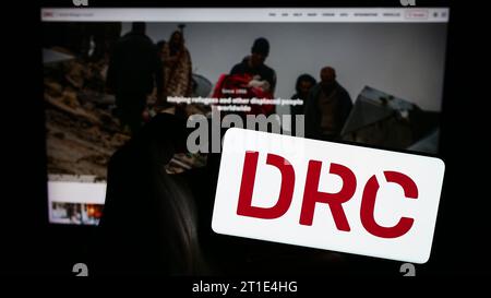 Personne tenant un téléphone portable avec le logo de l'organisation humanitaire Danish Refugee Council (DRC) devant la page Web. Concentrez-vous sur l'affichage du téléphone. Banque D'Images