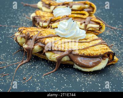 délicieuses crêpes fines avec tartinade au chocolat et tranches de banane, vue de côté Banque D'Images