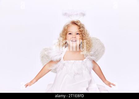 Belle, souriante, mignonne petite fille en robe blanche à l'image d'ange debout isolé sur fond de studio blanc Banque D'Images