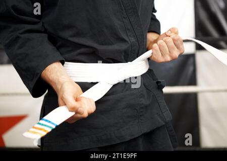 Homme, mains et ceinture blanche en karaté d'arts martiaux débutant, entraînement ou discipline au dojo. Gros plan d'une personne masculine liée gi ou se classant en soi Banque D'Images