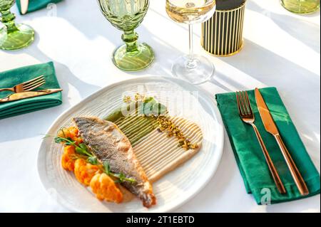 Filet de bar grillé avec chou-fleur, sauce et pistache. La nourriture repose sur une plaque en céramique légère sur une table dans un restaurant. Banque D'Images