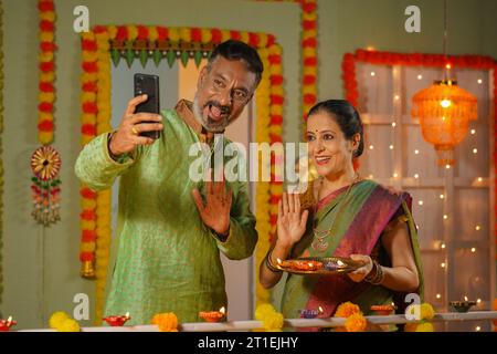 Couple senior parlant sur appel vidéo en utilisant smartphone pendant la célébration du festival diwali à la maison - concept de lien familial, culture traditionnelle et Banque D'Images