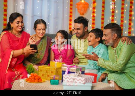 Groupe de famille mixte indienne heureuse voyant le téléphone portable pendant la célébration du festival de famille diwali - concept de réunions émotionnelles, lien relationnel Banque D'Images