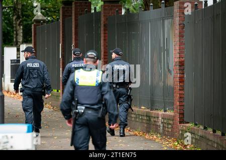 Hambourg, Allemagne. 13 octobre 2023. Les policiers marchent sur le trottoir devant la clôture de l'école juive Talmud Torah. Suite à l'attaque sans précédent du Hamas islamiste contre Israël et à l'opération militaire subséquente du pays dans la bande de Gaza, la police de Hambourg attend des manifestations pro-palestiniennes vendredi et a visiblement accru sa présence dans le centre-ville et devant les institutions juives. Crédit : Jonas Walzberg/dpa/Alamy Live News Banque D'Images