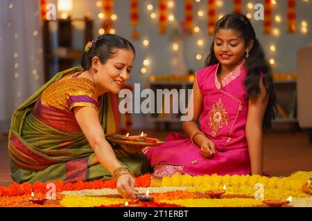 Grand-mère heureuse avec petit-enfant fille plaçant des lampes diya sur Flower rangoli - concept de préparation du festival diwali, rituel de Tradition ou coutume et Banque D'Images