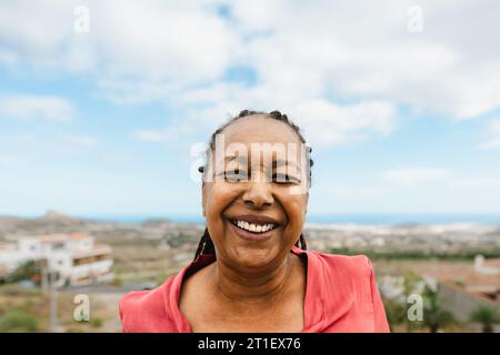 Heureuse femme africaine senior s'amusant souriant dans la caméra au toit de la maison Banque D'Images