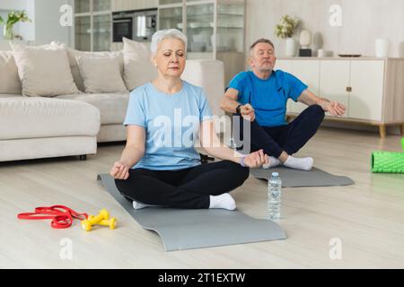 Méditation de pleine conscience de yoga. Couple adulte senior adulte pratiquant le yoga à la maison. La vieille femme de mari d'âge moyen assis dans lotus pose sur le tapis de yoga méditant la détente. Famille faisant la pratique de la respiration Banque D'Images