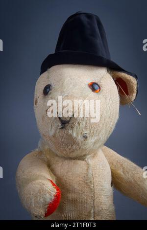 Un ours en peluche vieux et usé avec la plupart de sa fourrure disparue, portant un chapeau drôle noir Banque D'Images