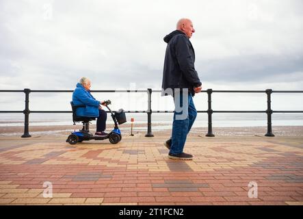 Une promenade en bord de mer pour un homme plus âgé avec une femme plus âgée à cheval sur un scooter de mobilité Banque D'Images