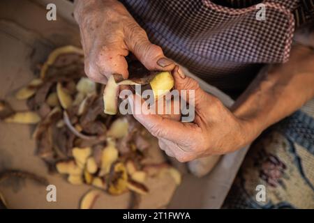 Les mains d'une femme âgée faisant des travaux domestiques de pelage des pommes de terre. Mains âgées avec problèmes articulaires, arthrose. Banque D'Images