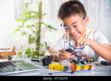 Un enfant asiatique branche le câble d'énergie et de signal à la puce de capteur avec la voiture robot Arduino Banque D'Images