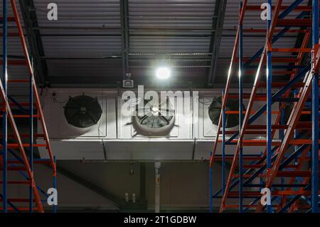 Un évaporateur frigorifique industriel à trois ventilateurs dans le congélateur d'un entrepôt frigorifique à cycle d'ammoniac. Étagères rouge et bleue illustrées. Banque D'Images