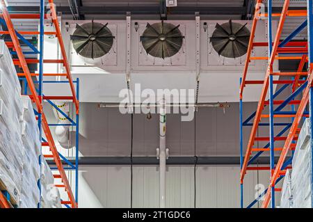 Un évaporateur frigorifique industriel à trois ventilateurs dans le congélateur d'un entrepôt frigorifique à cycle d'ammoniac. Étagères rouge et bleue illustrées. Banque D'Images