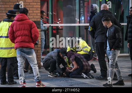 Broad Street, Birmingham, 13 octobre 2023 - deux membres du public et un policier s'occupent d'un fêtard vendredi 13 car ils sont devenus malades. - Revellers a frappé Broad Street à Birmingham vendredi 13 soir. Des centaines d'étudiants de l'Université de Birmingham se sont habillés en robe fantaisie avec le thème de tout ce qui commence par la lettre 'T' avec un groupe de filles portant une tenue Tampax et un autre groupe est venu comme un Tetley Tea Set alors qu'ils faisaient la fête toute la nuit dans Heidi's Bier bar un étudiant s'est déguisé en tube de dentifrice et un autre en «Tabloid journal». Tempera Banque D'Images