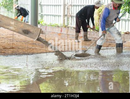 Les travailleurs nivelent le béton coulé sur le sol dans le chantier de construction. Banque D'Images