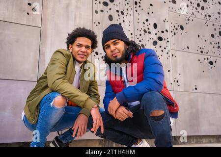 Style urbain, portrait de deux amis noirs latino s'amusant dans la rue. Garçon de cheveux afro, garçon brunette avec les cheveux longs avec chapeau Banque D'Images