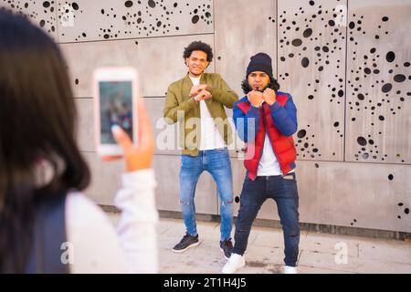 Style urbain, deux gars enregistrant une vidéo pour les réseaux sociaux, deux amis noirs latinos qui s'amusent dans la rue. Garçon de cheveux afro, garçon brunette avec long Banque D'Images