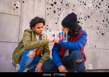 Style urbain, portrait de deux amis noirs latino s'amusant dans la rue. Garçon de cheveux afro, garçon brunette avec les cheveux longs avec chapeau Banque D'Images