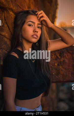 Une jeune jolie brune Latina avec de longs cheveux droits dans un T-shirt noir court et un pantalon rose. Portrait de la femme appuyée sur une sculpture avec croûte Banque D'Images