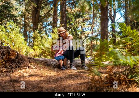 Portrait d'une mère avec son fils assis sur un arbre dans la nature à côté de pins Banque D'Images