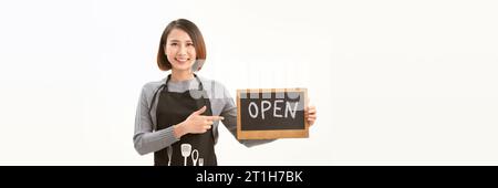 Femme propriétaire d'entreprise dans le tablier tenant le signe OUVERT et souriant isolé sur fond de bannière blanche Banque D'Images