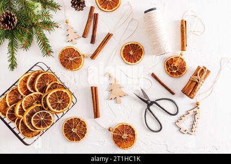 Vue de dessus de fond texturé blanc avec guirlande maison d'oranges séchées, branches d'épinette, tranches d'orange et ciseaux artisanaux. Pose à plat. décoration Banque D'Images