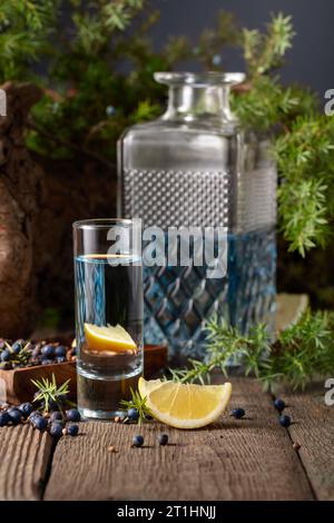 Branches de gin bleu et de genévrier sur une vieille table en bois. Gin avec des ingrédients - baies de genièvre, graines de coriandre et tranches de citron. Banque D'Images