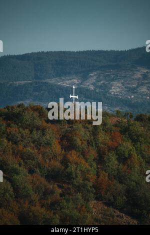 Une croix blanche chistienne au sommet d'une montagne avec une autre grande montagne en arrière-plan. Banque D'Images