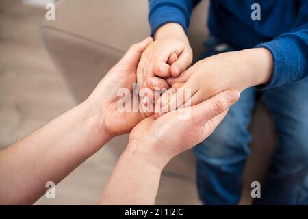 Close up jeune parent d'accueil compatissant tenant la main d'un petit garçon, donnant une aide psychologique, soutenant à la maison. Generatio différente sincère Banque D'Images