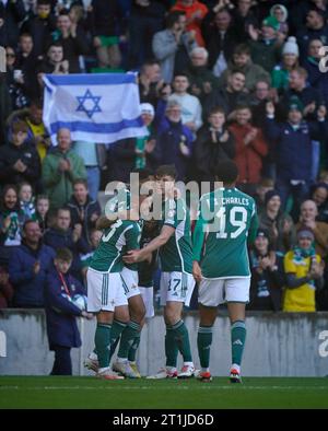 Josh Magennis (deuxième à gauche), d'Irlande du Nord, célèbre avec ses coéquipiers après avoir marqué le deuxième but du match, alors que les supporters brandissent un drapeau israélien dans les tribunes lors du match de qualification de l'UEFA Euro 2024 du Groupe H au Windsor Park, Belfast. Date de la photo : Samedi 14 octobre 2023. Banque D'Images