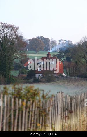 Une maison dans la campagne britannique chauffée en brûlant du bois comme la fumée sort de la cheminée polluant l'environnement à une époque de changement climatique, le gaz Banque D'Images