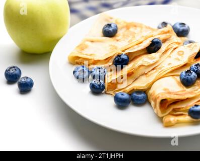 Crêpes fines avec des myrtilles fraîches dans une assiette sur une table blanche. Banque D'Images