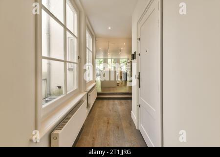 un long couloir étroit avec des murs blancs et du parquet, la pièce est bien éclairée par la lumière venant à travers la fenêtre Banque D'Images