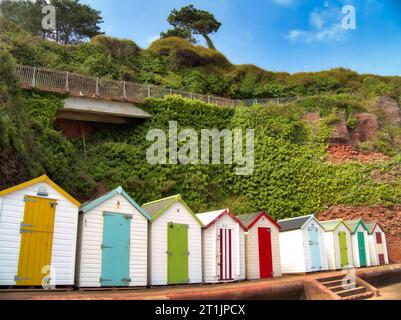 Une rangée de cabanes de plage avec leurs portes colorées sur la promenade de Goodrington North Sands en dessous de la falaise Walk de Roundham Head, Paignton. Banque D'Images