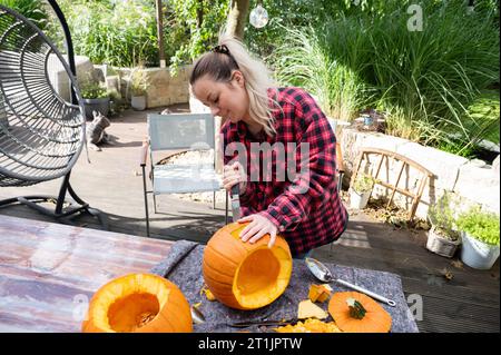 Pour Halloween, une femme blonde coupe un visage dans une citrouille orange avec un chevalier Banque D'Images