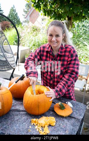 Femme blonde creusant et enlevant les graines des citrouilles comme décoration pour la saison d'Halloween Banque D'Images