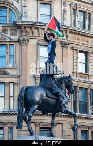 Westminster, Londres, Royaume-Uni. 14 octobre 2023. Une manifestation a lieu contre l'escalade de l'action militaire dans la bande de Gaza alors que le conflit entre Israël et le Hamas se poursuit. Organisés par des groupes tels que Palestine Solidarity Campaign et Stop the War Coalition, intitulés « manifestation nationale : Marche pour la Palestine » et avec des appels à « mettre fin à la violence » et à « mettre fin à l’apartheid », les manifestants se sont rassemblés devant la BBC à Portland place avant de se diriger vers Whitehall et Trafalgar Square. Manifestant sur la statue équestre de Charles Ier avec drapeau Banque D'Images