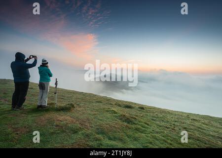 Un couple observe une inversion des nuages au lever du soleil sur MAM Tor dans le Derbyshire. Banque D'Images