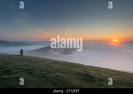 Un photographe observe une inversion des nuages au lever du soleil sur MAM Tor dans le Derbyshire. Banque D'Images