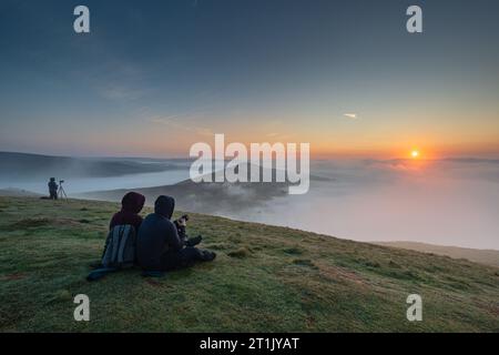 Un couple observe une inversion des nuages au lever du soleil sur MAM Tor dans le Derbyshire. Banque D'Images