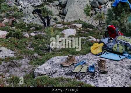 Matériel de séchage après une randonnée au camping. Vieilles bottes de trekking brunes, semelles vertes et chaussettes bleues à sécher après une journée de randonnée, disposées sur pierre. W Banque D'Images