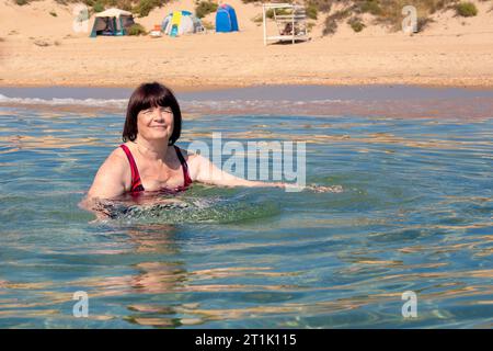 Une femme plus âgée nage dans de l'eau de mer claire. Vacances à la mer sur le rivage. Banque D'Images