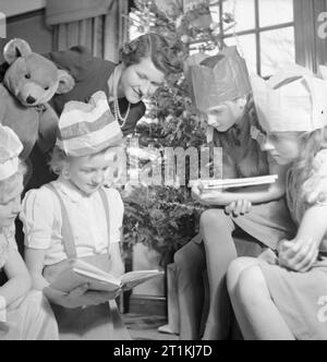 Fête de Noël pour le Cavalier Devereux's Daughter- Noël en temps de guerre, Pinner, Middlesex, décembre 1944 douze ans Jean Devereux lit un livre, elle a reçu comme cadeau de Noël à son domicile à Pinner, comme sa mère et plusieurs de ses amis. Un grand ours en peluche peut être vu sur la gauche de la photographie. La légende originale précise que cette dans un vieux ours en temps de paix, et n'était pas un cadeau de Noël, que de tels jouets ne sont plus accessibles. Derrière eux on peut voir l'arbre de Noël est un présent de l'époux de Mme Devereux, actuellement en service dans l'armée à l'étranger. L'arbre était bon de Banque D'Images