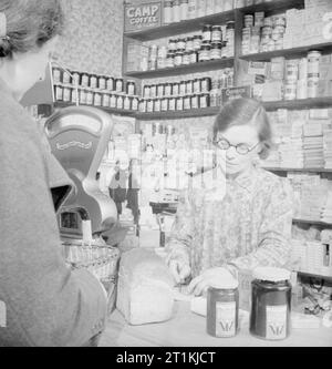 Le jardinage communautaire- Production alimentaire en temps de guerre à Rowney vert, Worcestershire, Angleterre, RU, 1943 Mme Forsyth recueille sa ration de confiture à la boutique dans le village de Rowney vert dans le Worcestershire, comme le commerçant vérifie les coupons dans le livre de Mme Forsyth ration. La confiture est faite par les femmes de l'institut féminin local dans la salle des fêtes. Banque D'Images